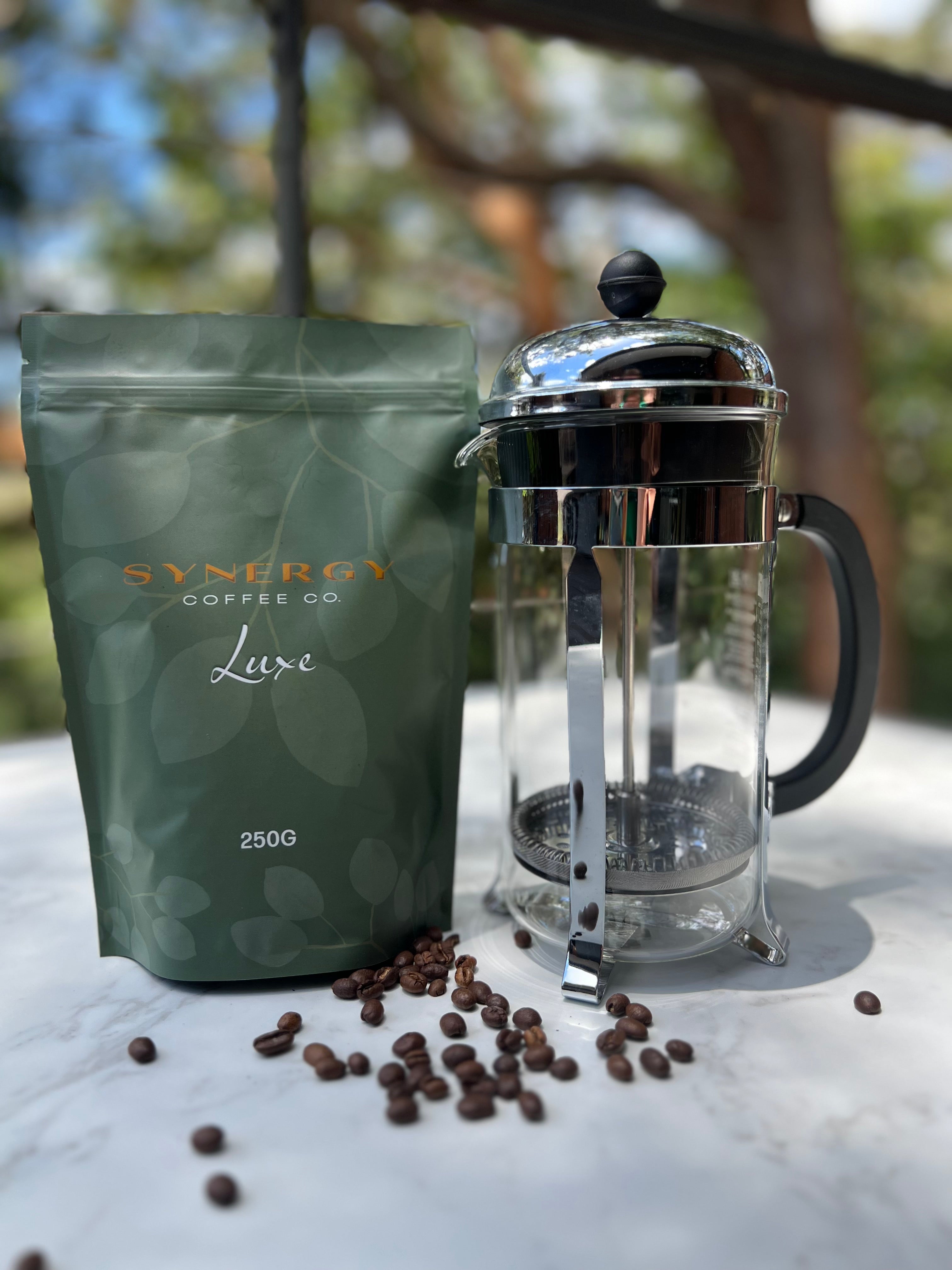 Synergy Coffee Co. coffee package with a French press and coffee beans on a blurred natural background